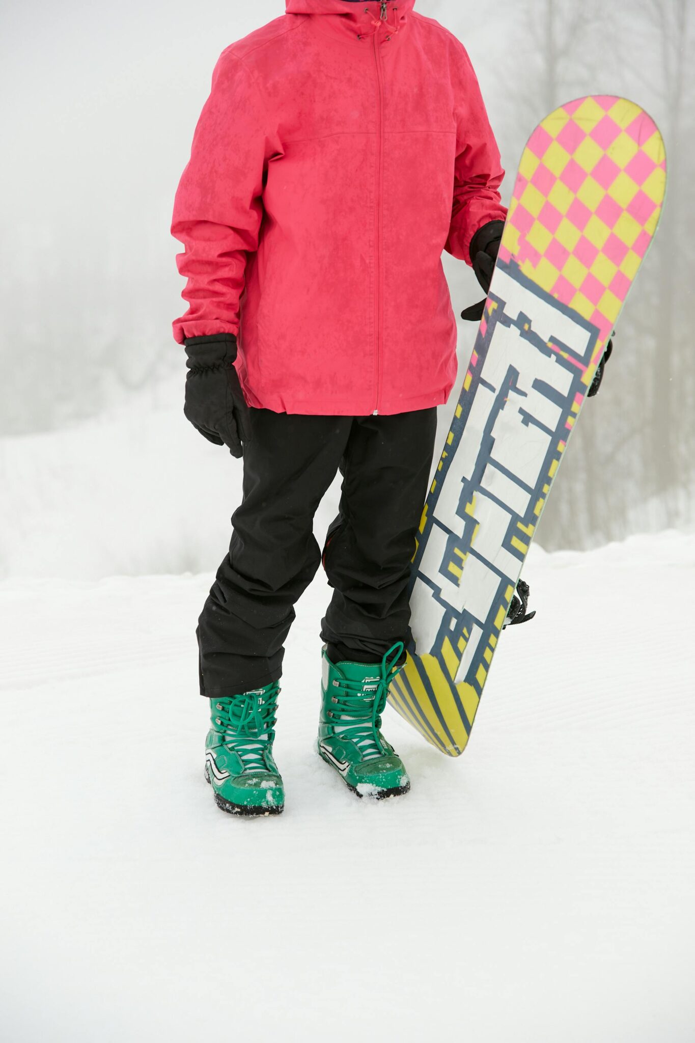 Person in winter clothing holding a snowboard in a snowy landscape.