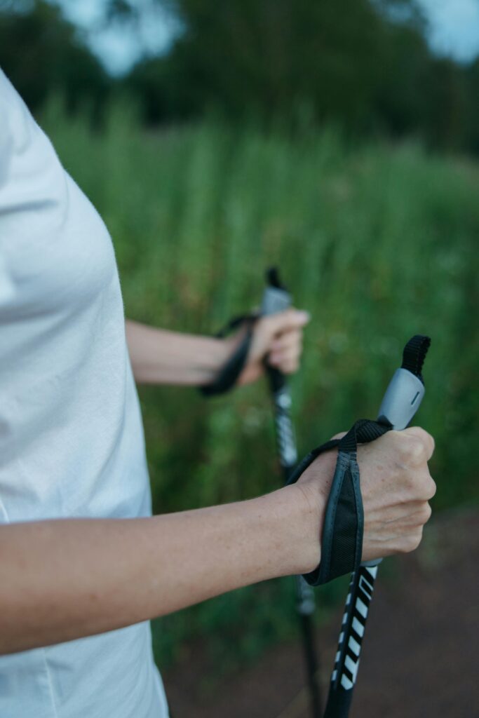 Close-up of a woman holding trekking poles, surrounded by lush greenery, outdoors.